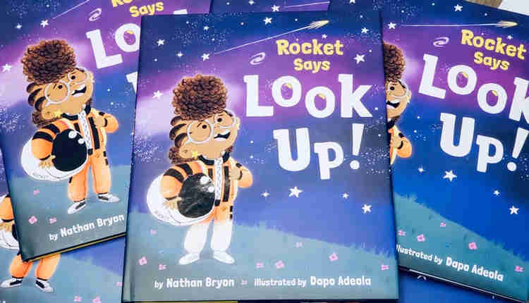 Photograph of a pile of copies of the book Rocket Says Look Up written by Nathan Bryon and illustrated by Dap Adeola