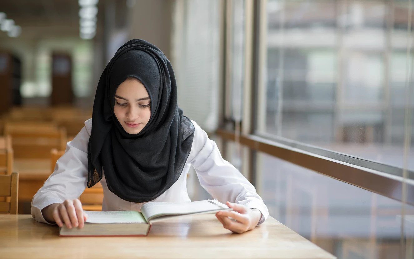 Image of a student with a hijab reading a textbook